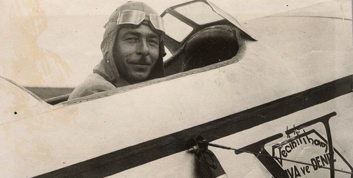 Vecihi Hürkuş smiling from the cockpit of an aircraft, wearing a flying helmet and goggles